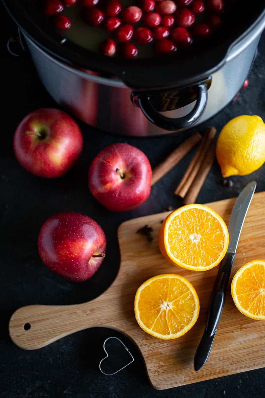 A slowcooker with holiday wassail, along with oranges cut horizontally for decoration.