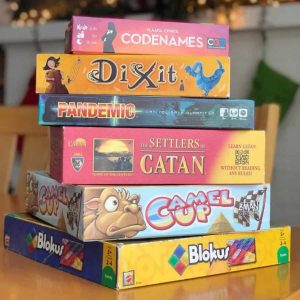 A stack of family board games to buy for Christmas in front of holiday twinkle lights.