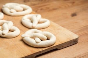 A bunch of soft pretzels sitting on a cutting board unbaked.