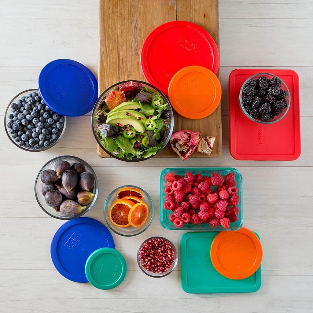 A set of the glass food storage containers with strawberries, blueberries, salad, and veggies in them surrounded by lids.