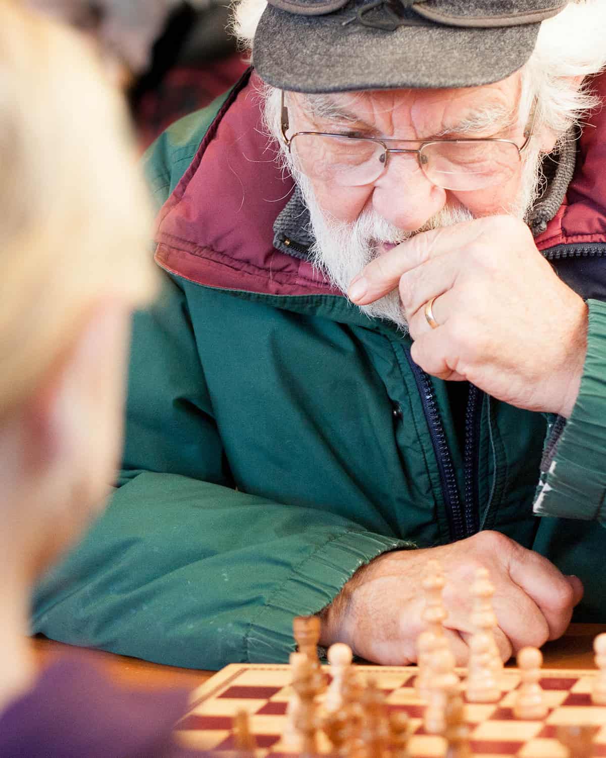 A grandpa thinking as he is playing chess with his granddaughter at a coffee shop.