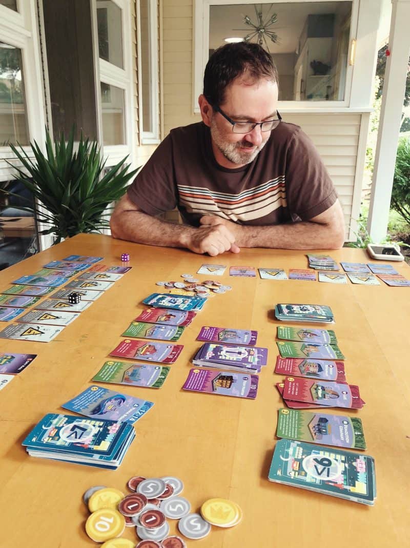 A father enjoying a game of Machi Koro outside with his family.