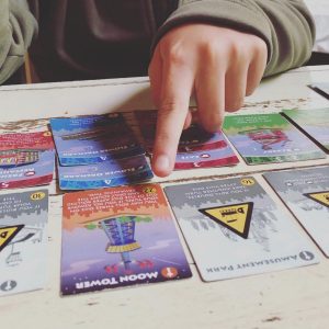 A child pointing to her winning card in the game Machi Koro.