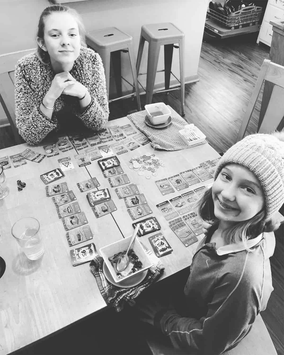 Two teen friends happily playing Machi Koro together.