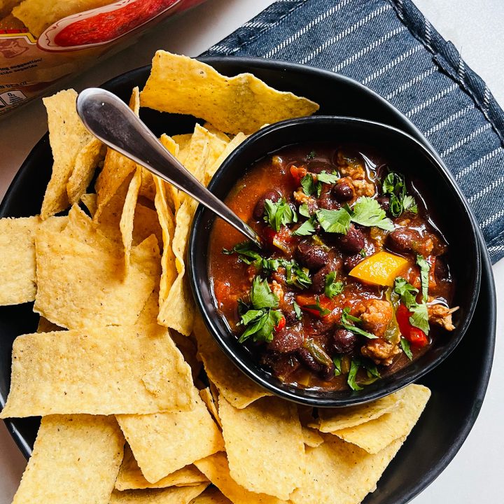 A bowl of turkey chili sound with tortilla chips sitting on a hot pad.