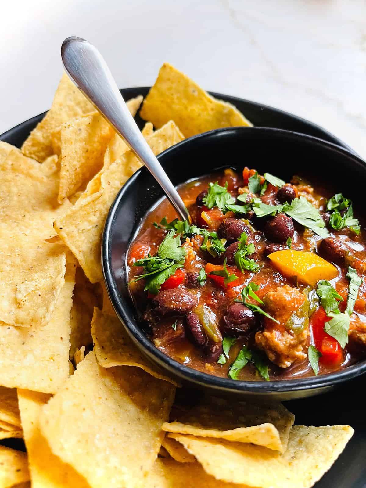 A bowl of turkey taco soup with a spoon being served with tortilla chips.