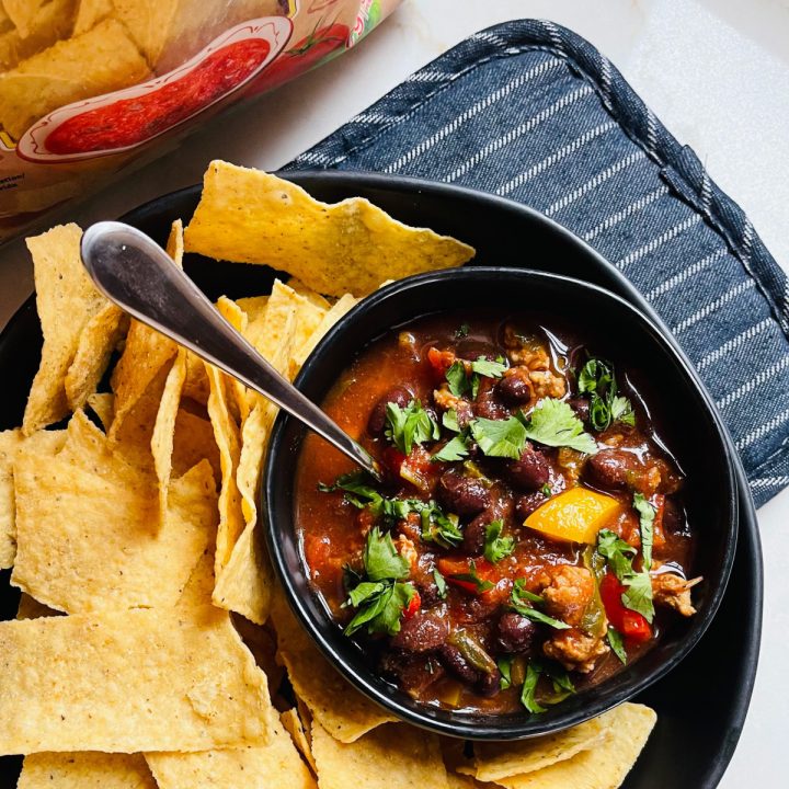 A bowl of turkey chili served with tortilla chips sitting on a hot pad.