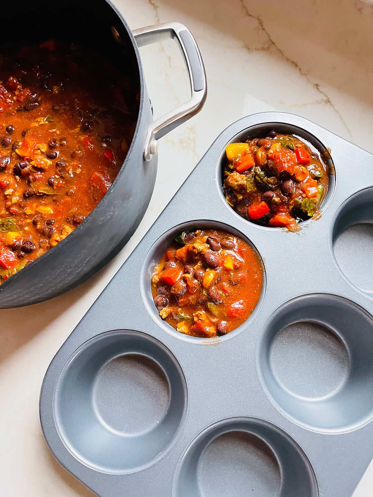A stovetop pot of turkey taco soup next to a muffin tin to freeze single servings.