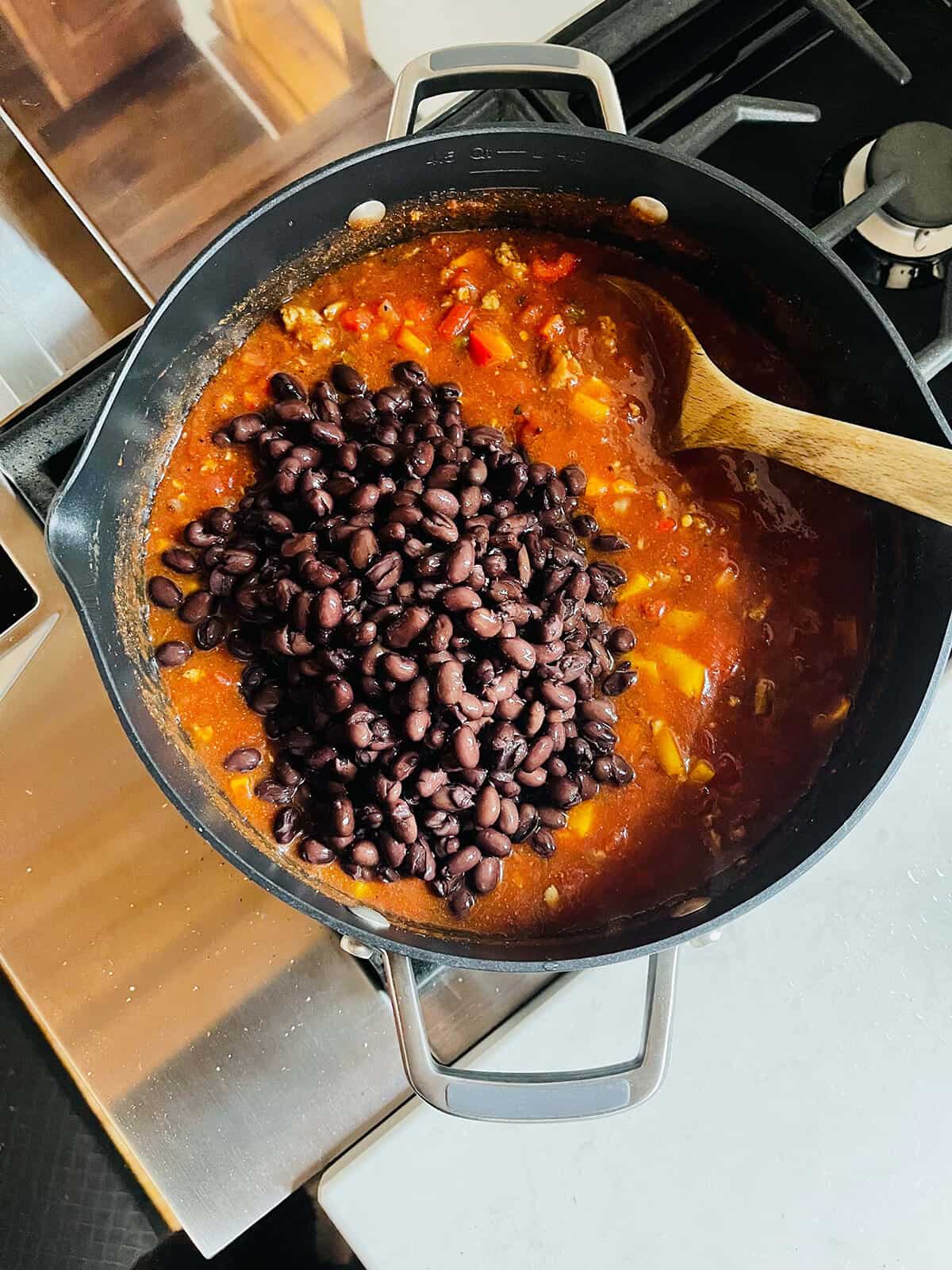 A stovetop pot of turkey taco soup with black beans being stirred in.