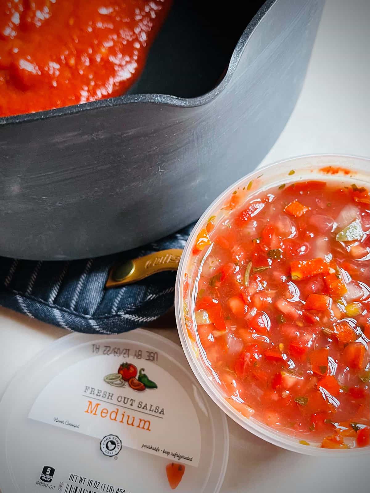 A soup pot with a container of fresh cut salsa next to it.