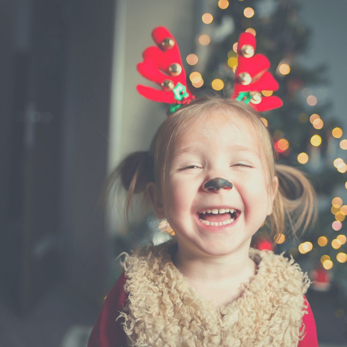 Little girl wearing antlers with a painted reindeer nose laughing as she hears Would You Rather Christmas questions.